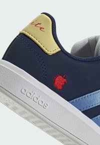 Donkerblauwe Adidas sneaker met witte zool, lichtblauwe strepen, gele hielkap met rode tekst, en een kleine rode geborduurde appel aan de zijkant.