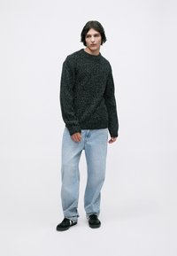 Sweter z dzianiny w kolorze czarnym i szarym o teksturowanym wykończeniu, z okrągłym dekoltem, długimi rękawami, połączony z jasnoniebieskimi luźnymi dżinsami i czarnymi butami.