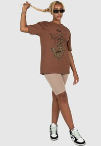 Brun grafisk t-shirt med sommerfugledesign, parret med beige cykelshorts og sorte højhælede sneakers, har en afslappet pasform og korte ærmer.