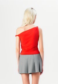 Top rojo de un solo hombro con detalle fruncido; combinado con una falda mini plisada gris. Tejido suave, diseño ajustado y textura en capas.