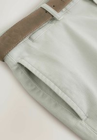 Pantalon gris clair texturé avec une ceinture en suède beige passée dans les passants de ceinture, mettant l'accent sur la poche supérieure et la zone de la taille.