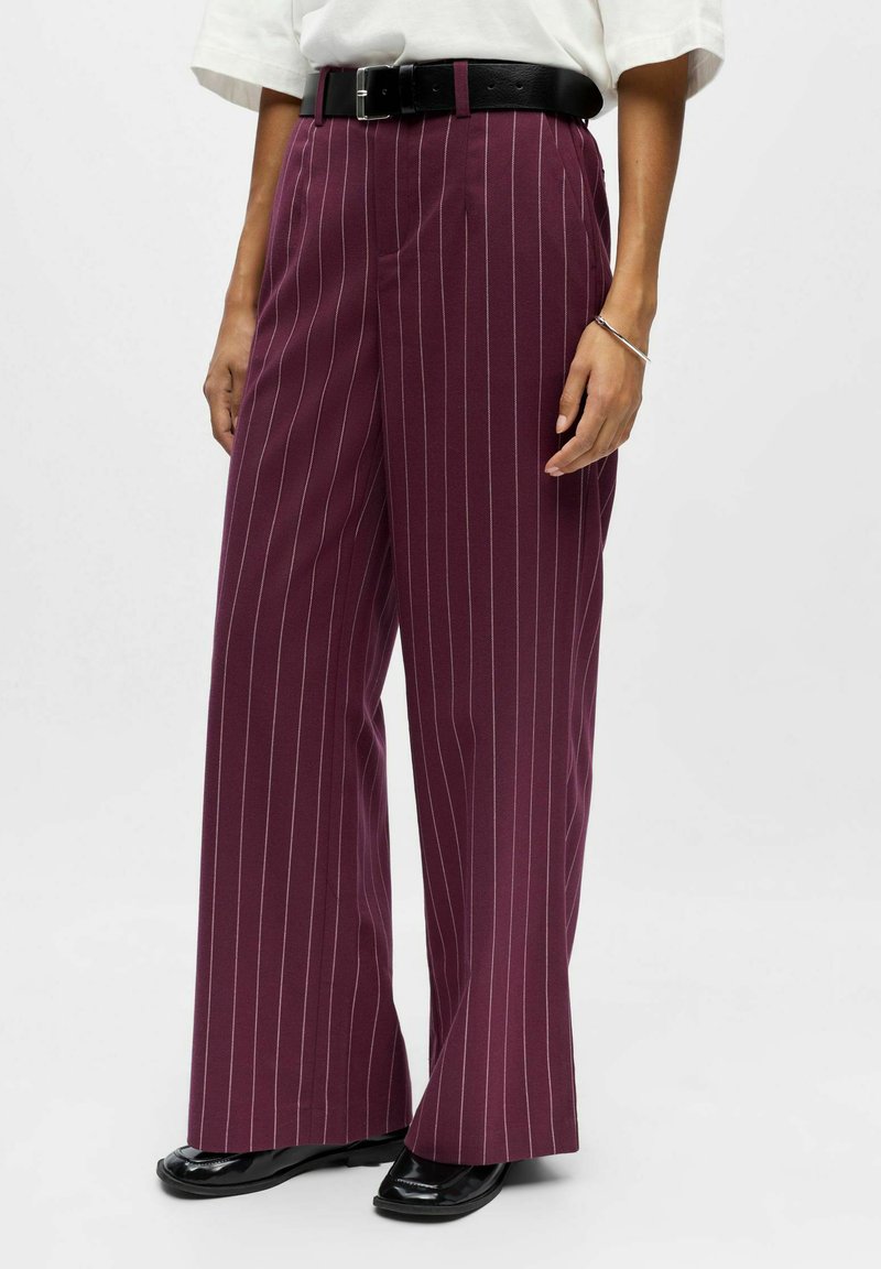 Pantalons bordeaux à jambes larges avec des rayures verticales blanches, fabriqués en tissu texturé, associés à une ceinture noire et des mocassins brillants.