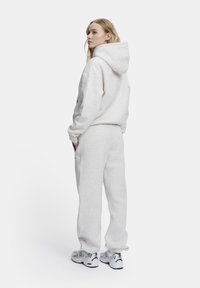 Ljusgrå bomullshuvtröja med en stor huva, tillsammans med matchande joggingsbyxor. Mjuk textur med ribbade muddarna, bärs med vita sneakers.