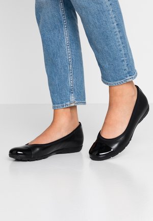 Czarne baleriny wykonane z gładkiej skóry z błyszczącym noskiem typu cap-toe. Charakteryzują się niskim profilowaniem i elastyczną podeszwą, zestawione z niebieskimi dżinsami.