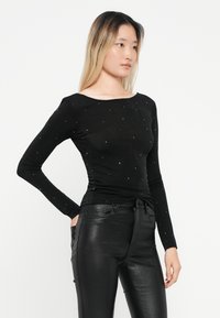 Zwarte longsleeve top van zacht materiaal, met een bateauhals en versierd met verspreide rhinestones voor extra detail.