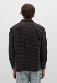 Bruin en zwart geruit overhemd met een relaxte pasvorm, lange mouwen en knoopmanchetten. Zacht materiaal, achteraanzicht, geen zichtbare logo's of ontwerpen.
