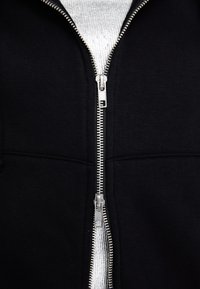 Felpa nera con zip caratterizzata da una cerniera argentata, texture del tessuto a costine e interno grigio a contrasto. Tessuto liscio senza motivi visibili.