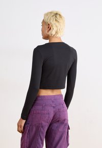 Top cropped preto de mangas longas com decote redondo, combinado com calças cargo roxas com dois bolsos traseiros. Textura de tecido suave.