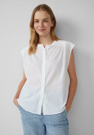 Blouse sans manches blanche avec un devant à boutons, présentant des coutures détaillées aux épaules et une coupe décontractée. En coton doux.