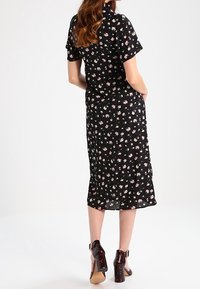 Black floral dress with short sleeves, mid-calf length, featuring a lightweight fabric and small colorful floral patterns. Heeled shoes.
