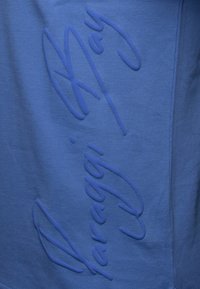 Blå texturerad tyg med präglad signaturdetalj, som har en slät yta och ett lätt upphöjt mönster.