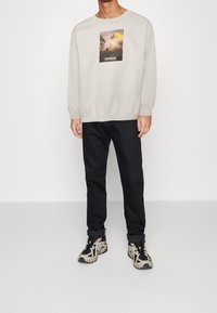 Sudadera gris claro con un gráfico de temática natural y el texto "montana", combinada con pantalones negros y zapatillas de patrón beige/negro.