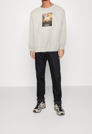Sudadera gris claro con un gráfico de temática natural y el texto "montana", combinada con pantalones negros y zapatillas de patrón beige/negro.
