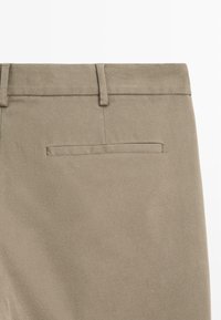 Khaki bukser med en glat tekstur, der har en bagfick med paspolering og bæltestropper, lavet af et holdbart vævet stof.