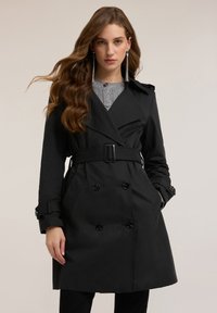 Czarny trencz wykonany z gładkiego materiału, z podwójnym rzędem guzików, paskiem w talii, dużymi guzikami i szerokimi klapami.