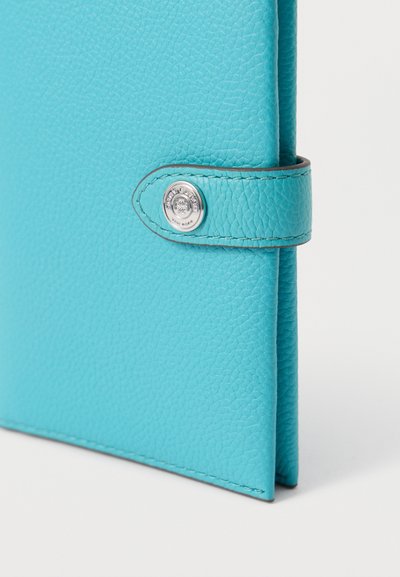 Turquoise leren notitieboekhoes met textuur, voorzien van een gestikte strip en een zilveren drukknoop met gegraveerde merkdetails.