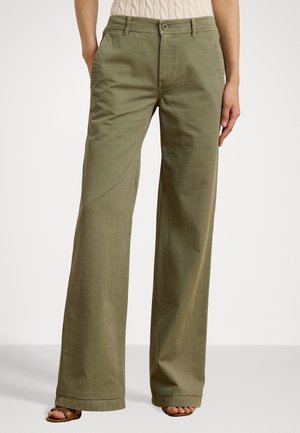 Pantalon large vert olive porté avec un haut en maille beige et des sandales marron à bout ouvert, les mains détendues le long du corps.
