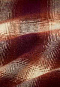 Close-up of soft fabric with a red, brown, and cream plaid pattern showing texture and folds.