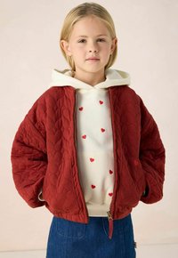 Rode gewatteerde jas met een grote capuchon, featuring een witte trui eronder versierd met kleine rode hartjes, gecombineerd met een denimrok.