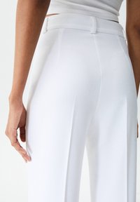 Białe spodnie o wysokim stanie z gładką fakturą, posiadające dopasowany krój, szlufki na pasek i zakładki wzdłuż nogawek dla uzyskania smukłego wyglądu.