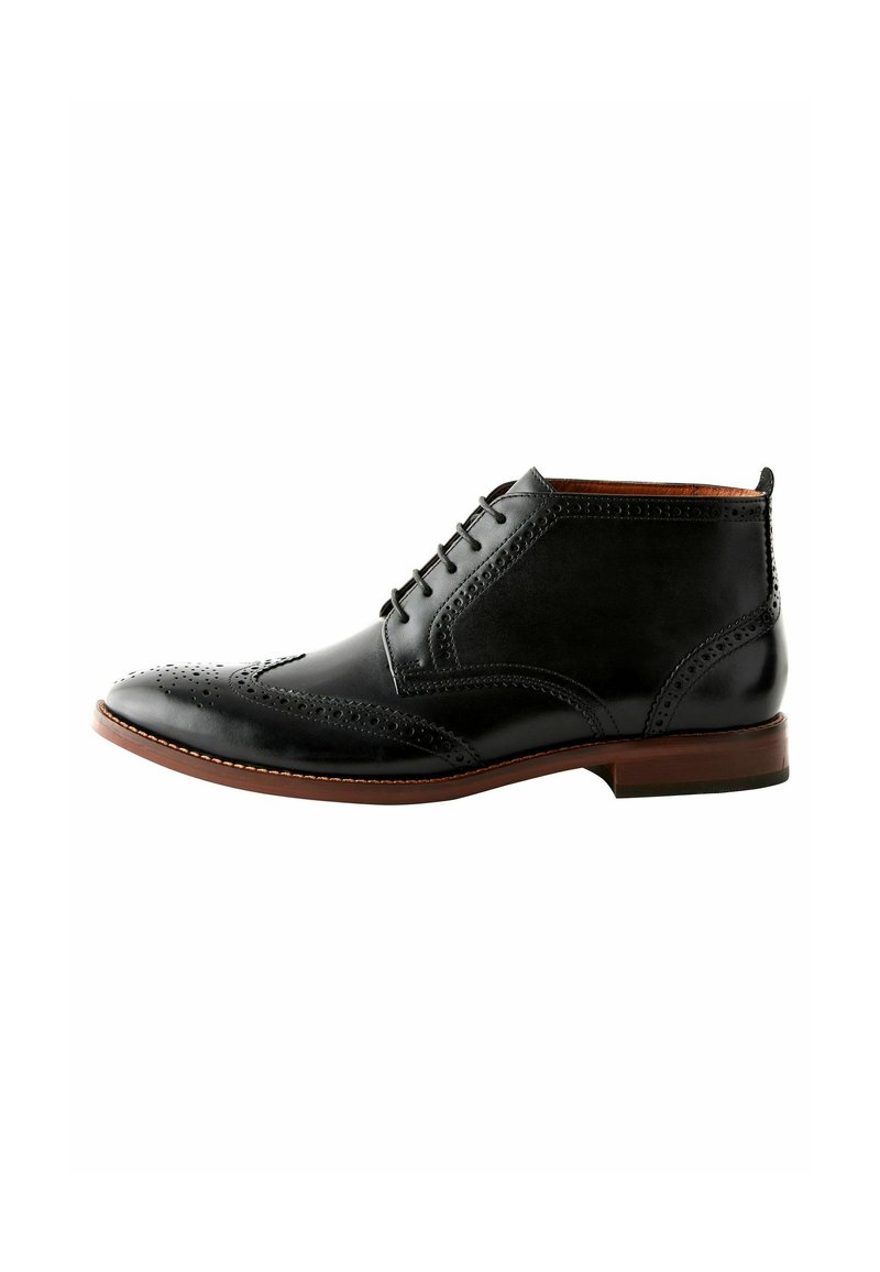 Botas de piel negras hasta el tobillo con detalles de brogue, cierre con cordones y suela contrastante en marrón. Textura suave con acabado pulido.