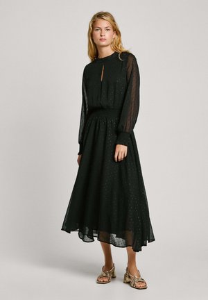Robe noire à manches longues avec un décolleté en trou de serrure, tissu texturé, taille froncée et jupe fluide. Portée avec des sandales à talons blocs métalliques.