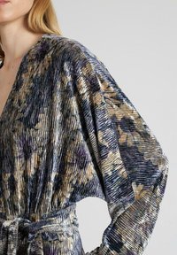 Vestido con estampado floral en tejido texturizado, que presenta tonos de púrpura, beige y negro, con mangas anchas y cintura anudada.