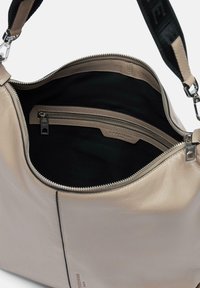 Beżowa torba skórzana z zamkiem błyskawicznym, przestronnym wnętrzem i czarnym wykończeniem. Posiada małą kieszeń na zamek oraz szeroki, regulowany pasek na ramię.