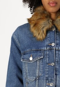 Denim jacket with a blue wash, featuring a faux fur collar in tan and brown. Metal buttons and two front pockets are visible.