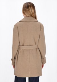 Beige wool coat with a belted waist, notched collar, and long sleeves. Smooth texture and knee-length design with a tailored fit.