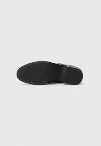 Black leather shoe with a smooth surface, round toe, and textured rubber sole. Features a slight heel and minimalistic design.