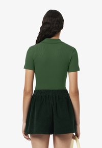 Grünes Poloshirt mit kurzen Ärmeln, gerippte Struktur; kombiniert mit dunkelgrünen Cordshorts mit elastischem Bund.