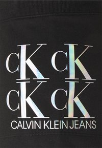 Černá látka s opakujícím se designem loga v irizujícím písmu: "ck" a "CALVIN KLEIN JEANS" psané velkými a malými písmeny.
