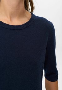Námořnická modrá pletená blůza s kulatým výstřihem a krátkými rukávy, která má jemnou texturu a přiléhavý střih.