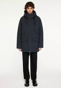 Donkerblauwe parka-jack met een capuchon, voorzien van twee voorkruiszakken, een drukknopen sluiting aan de voorkant en een losse pasvorm. Gemaakt van een gladde, textuurstof.