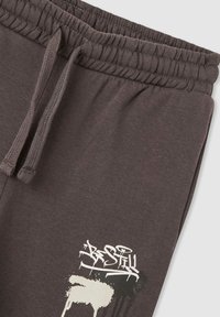 Ciemnoszare dresy z elastycznym pasem, sznurkiem do regulacji i graficzną aplikacją w stylu graffiti "Bądź cicho" w jasnych kolorach w pobliżu kieszeni.