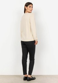 Maglietta a maniche lunghe color crema con vestibilità rilassata, abbinata a jeans neri aderenti e scarpe nere basse. Design semplice, senza motivi o dettagli.