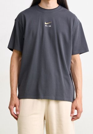 T-Shirt mit kurzem Arm und Rundhalsausschnitt aus dunkelgrauer Baumwolle, mit zentralem Nike-Logo in Beige. Lockerer Schnitt, glatte Textur, minimalistisches Design.