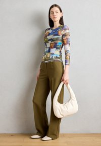 Top a maniche lunghe multicolore con design di cartoline, abbinato a pantaloni larghi verde oliva e una borsa morbida color crema.