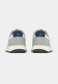 Szürke sportcipők texturált talppal, réteges kialakítással, kék és fehér kontrasztos díszítéssel a sarokrészen, és párnázott szegéllyel.