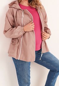 Lightweight, mauve zip-up jacket with a hood, elastic cuffs, and side pocket, layered over a pink top, paired with blue jeans.