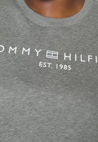 Sudadera de algodón gris con cuello redondo, que presenta el texto "TOMMY HILFIGER EST. 1985" y un logo rectangular en blanco.