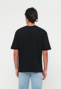 Camiseta de algodón negra con cuello redondo y mangas cortas. Corte holgado y diseño minimalista, sin logotipos ni adornos visibles.