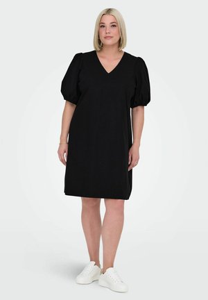 Zwarte jurk met pofmouwen, V-hals en knielange snit, gemaakt van zachte stof; gecombineerd met witte sneakers voor een casual uitstraling.