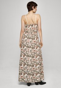 Maxikjole med blomstermønster, har tynne stropper, rynket rygg, lett stoff med grønne og rustfargede detaljer, ankellang, kombinert med svarte støvler.