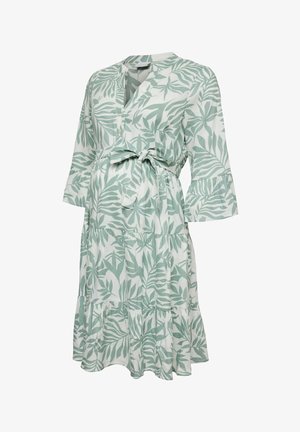 Hvid knælang kjole med grønne bladprint, V-hals, trekvartlange ærmer med flæser og et bindebælte i taljen.