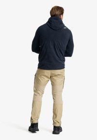 Navy Fleece-Hoodie mit hohem Kragen, kombiniert mit hellbeigen cargo-Hosen mit Seitentaschen und schwarzen Wanderschuhen.