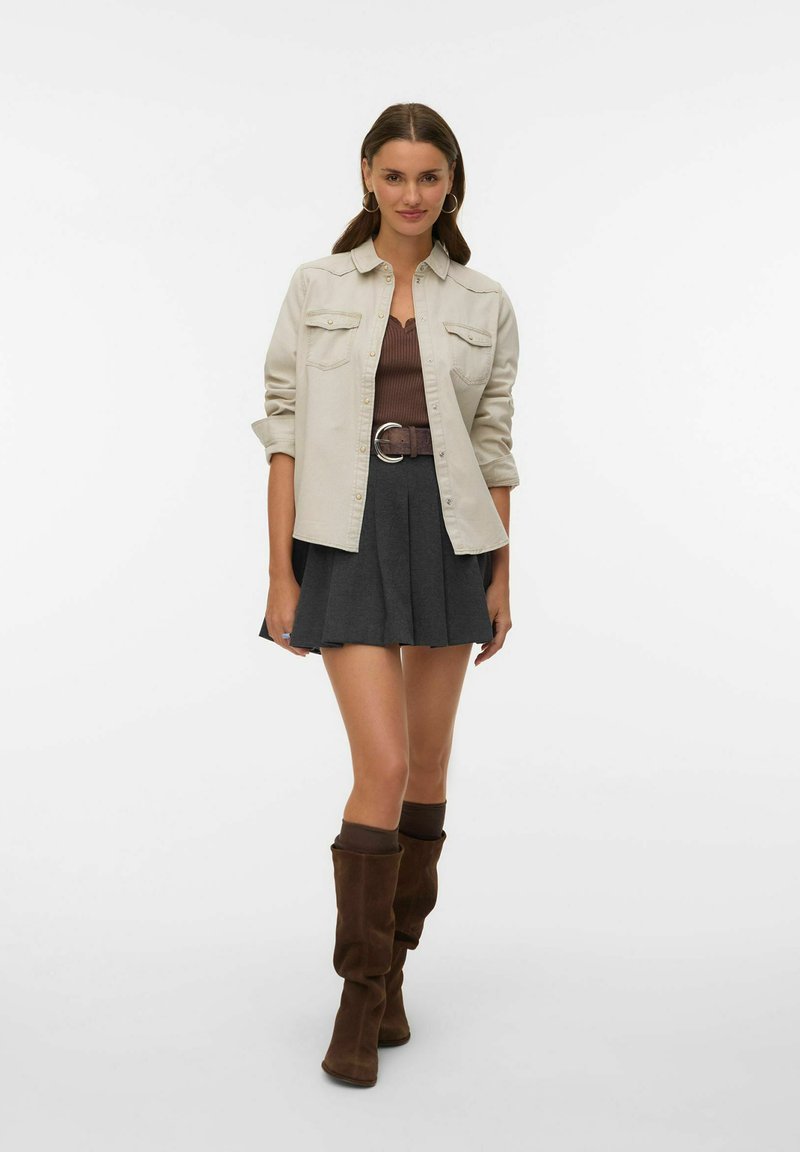 Beżowa koszula na guziki, brązowy prążkowany top, szara plisowana spódnica, brązowy pasek z okrągłą klamrą oraz luźne brązowe kozaki za kolano.