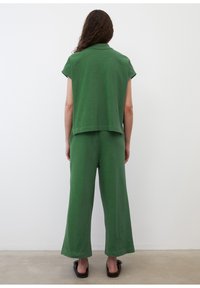 Ensemble vert deux pièces comprenant un haut à manches courtes et un pantalon à jambes larges, tous deux confectionnés dans un tissu doux à la texture lisse.