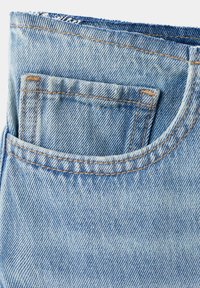 Gros plan sur un jean en denim bleu clair montrant une poche avant avec une couture orange détaillée et une petite poche intérieure pour pièces de monnaie.